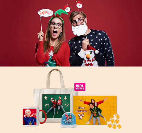 Junges Paar posiert mit Weihnachtsrequisiten, darunter BIPA Fotoshop Geschenkideen wie Tasse, Puzzle oder Schneekugel.
